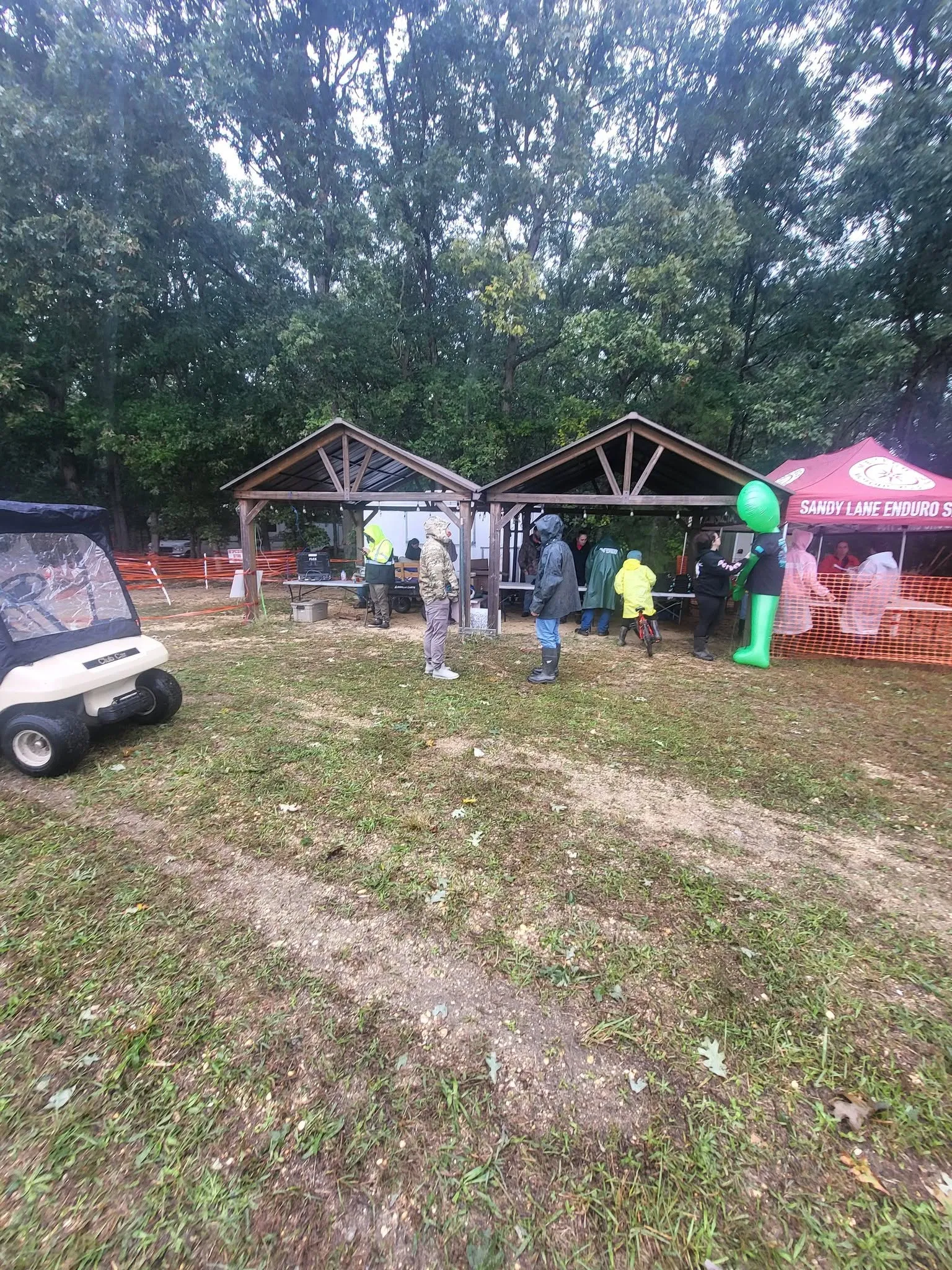 Riders and volunteers in rain gear gathered under pavilions at a wet, overcast event site